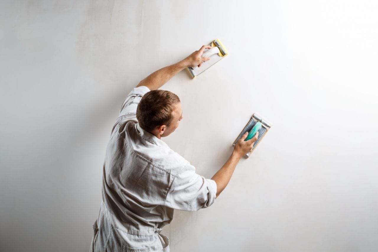 worker grinding white wall with sandpaper